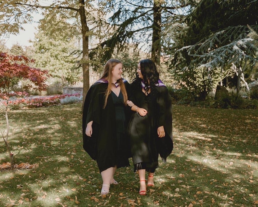 A photograph of 2022 graduates, Catia and Hannah, in their graduation robes and smiling at each other