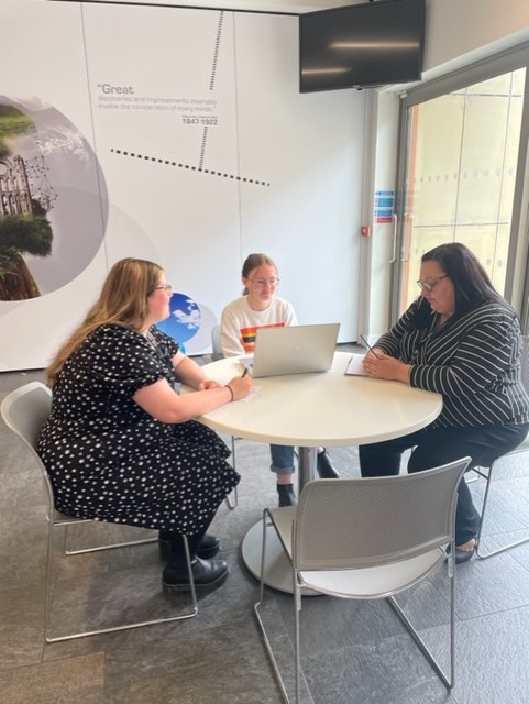 Photo of Siobhan, our career ready intern in 2022, sat at a table in a meeting with Alanna from Marketing and Lorna from Events