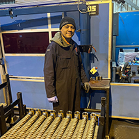 Photo of Hansley next to hydraulic machinery. He is wearing overalls.