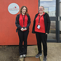 Photo of Niamh and her supervisor next to the Ladybird Nursery. They are both wearing a red uniform.