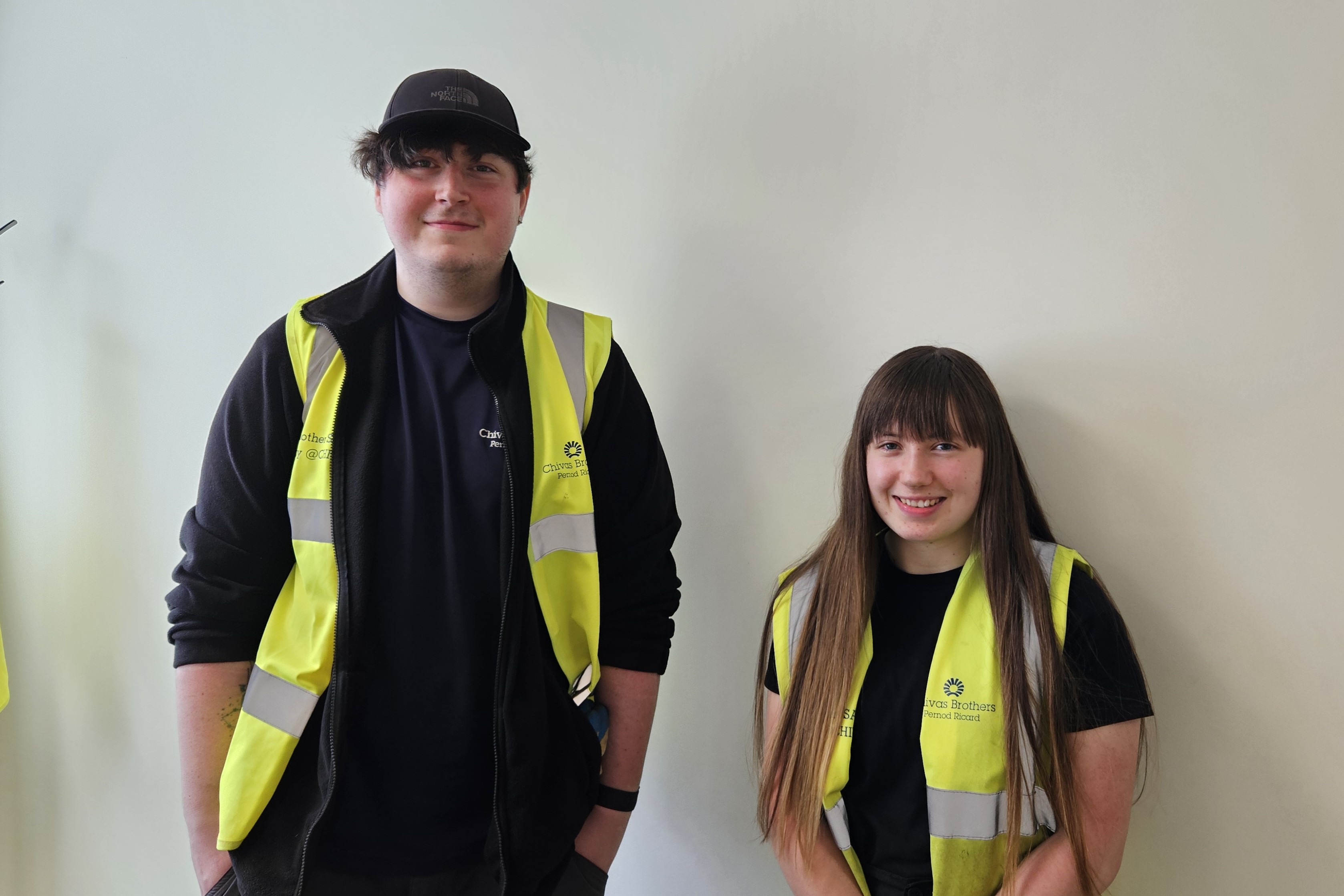 Photograph of employability clients, Dylan and Lucy, smiling at the camera and wearing hi-viz jackets in their place of work - Chivas Photograph of employability clients, Dylan and Lucy, smiling at the camera and wearing hi-viz jackets in their place of work - Chivas