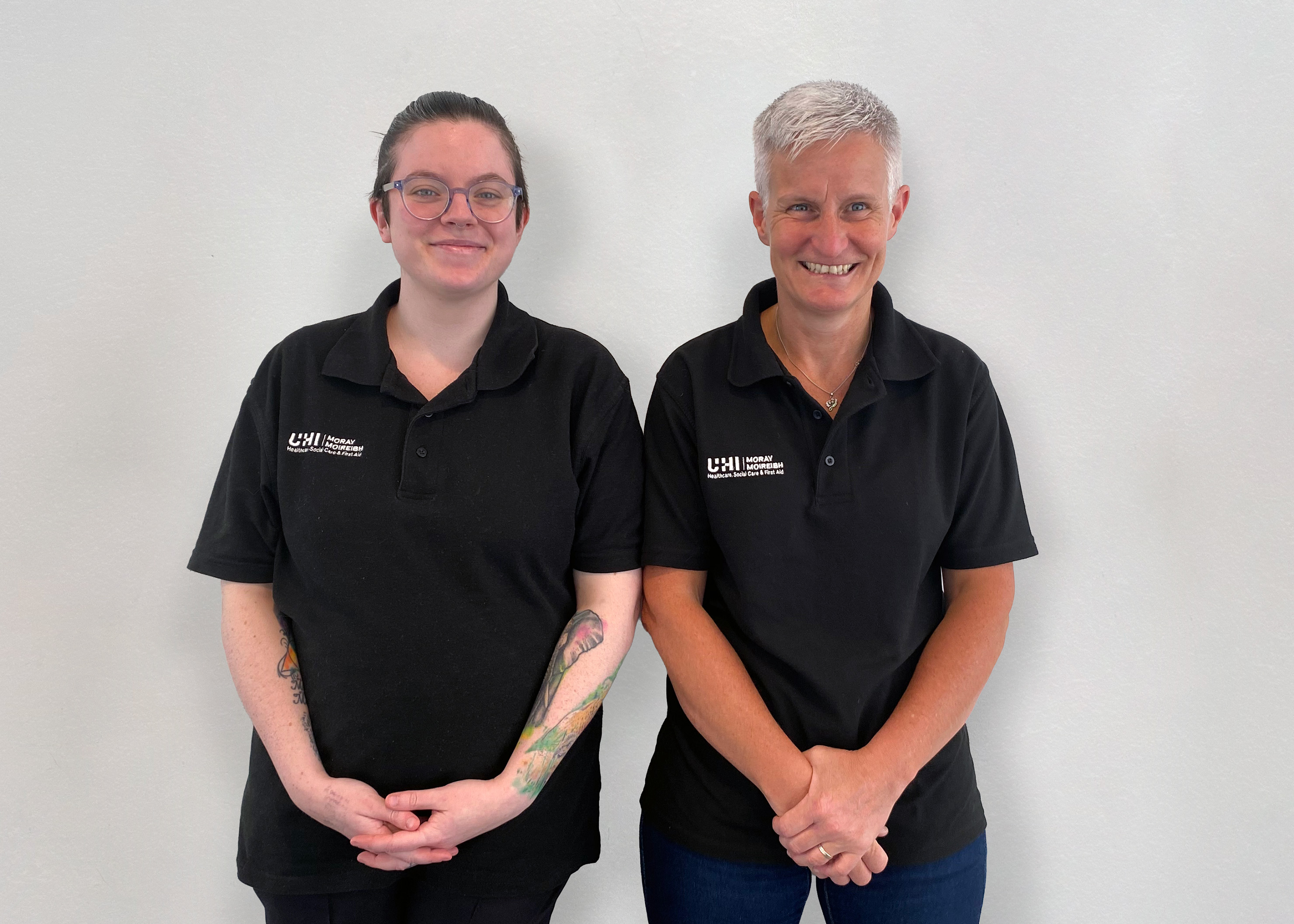 Two professional looking first aid trainers stood beside each other smiling at the camera.