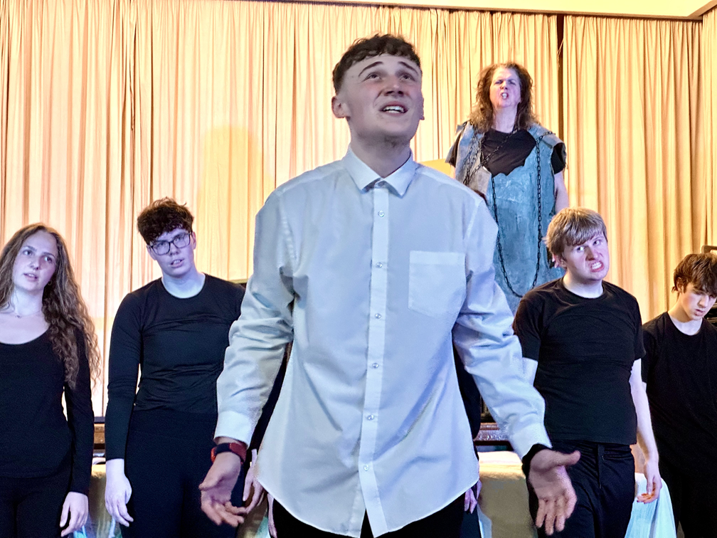 Photo of DJ acting in a show surrounded by fellow actors in the background