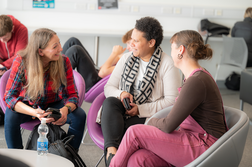 Photo of three female students sitting in the Moray Street social space chatting to eachother