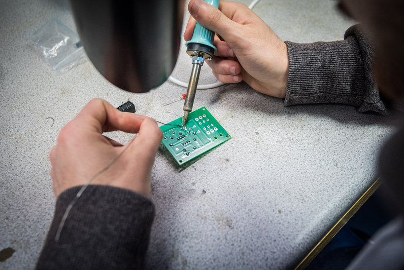 Photo of someone soldering a small motherboard Photo of someone soldering a small motherboard