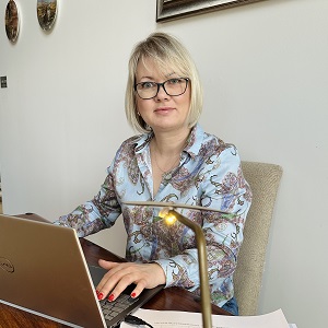 A headshot of HNC/D student, Victoria Waller, sat at a desk on her laptop and smiling at the camera